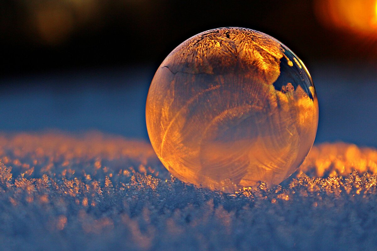 Close-up shot of a frozen bubble with warm reflections resting on a snowy surface at twilight.