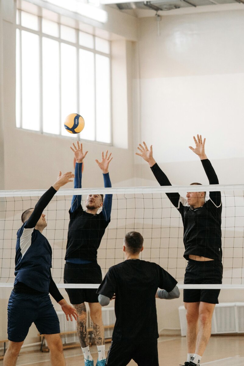 Dynamic indoor volleyball match with athletes jumping to block a ball over the net.