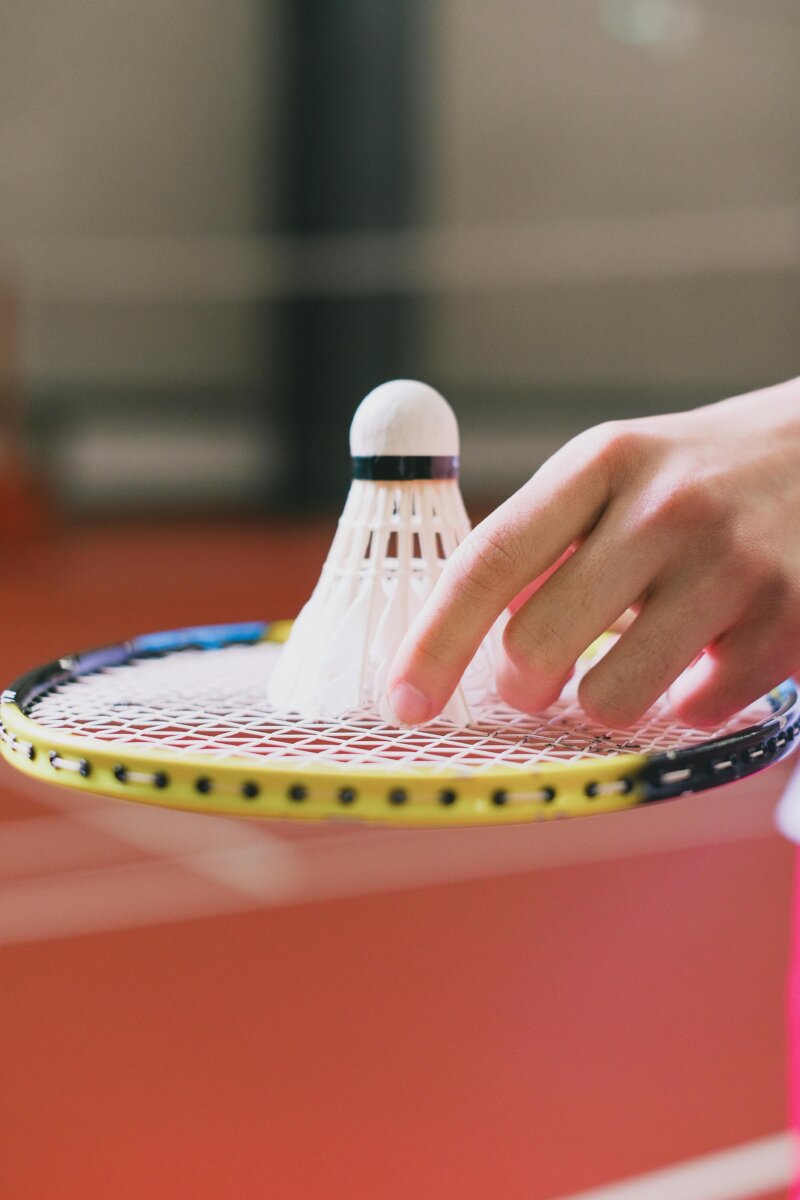 Close-up of a hand placing a shuttlecock on a badminton racket indoors.